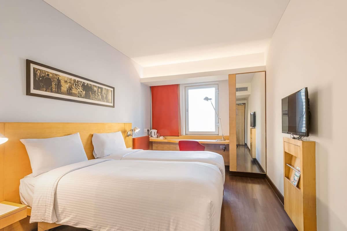 A hotel room with two beds, a desk, a chair, a TV, and a painting on the wall.