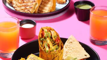 A table with a variety of food items including grilled sandwiches, a wrap, and a bowl of chips, along with glasses of orange juice.