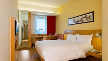 A hotel room with a bed, bedside table, lamp, and a desk with a chair.