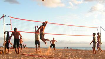 Ein Beachvolleyballspiel mit Spielern in Shorts und T-Shirts, einem Volleyballnetz und einem Sandstrand bei blauem Himmel.