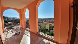 Un balcón con mesa y sillas, que ofrece vistas a un pueblo y montañas.