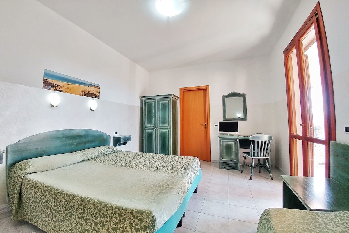 A bedroom with a bed, a desk, a chair, a wardrobe, and a door.