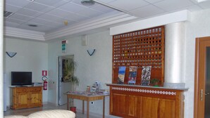 Un vestíbulo con un mostrador de recepción de madera, un televisor sobre un mueble, un extintor y un suelo estampado.