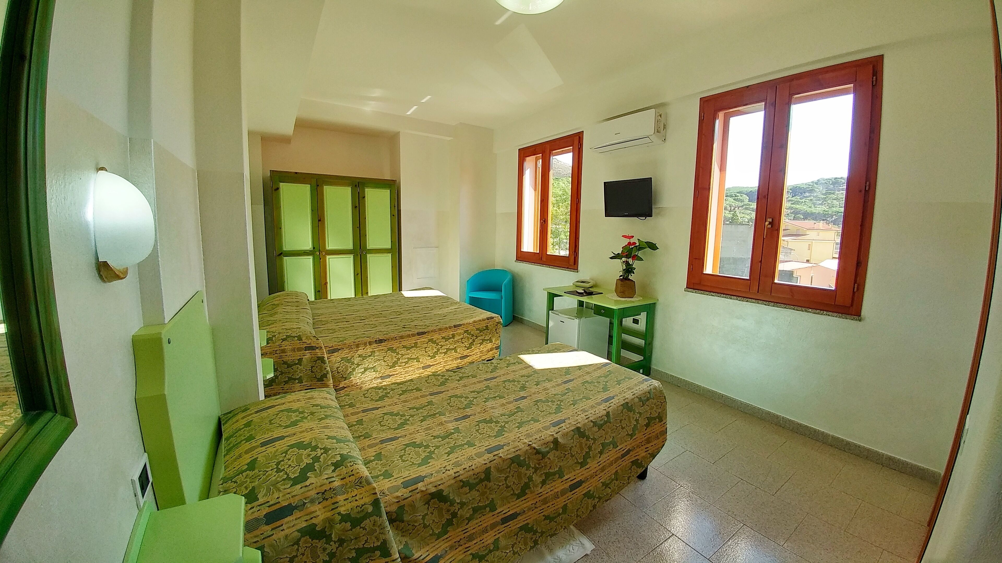 A bedroom with a bed, a desk, a chair, a TV, and a window with a view.
