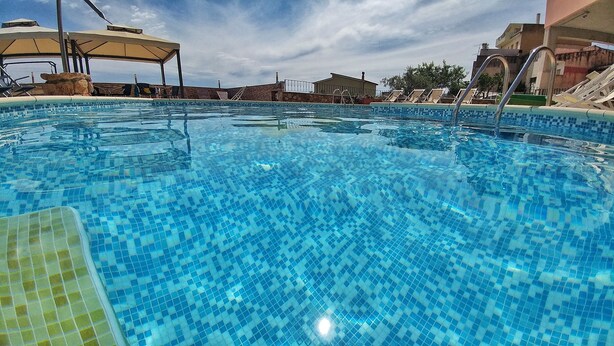 Una piscina con suelo de baldosas, rodeada de sillas de descanso y sombrillas.