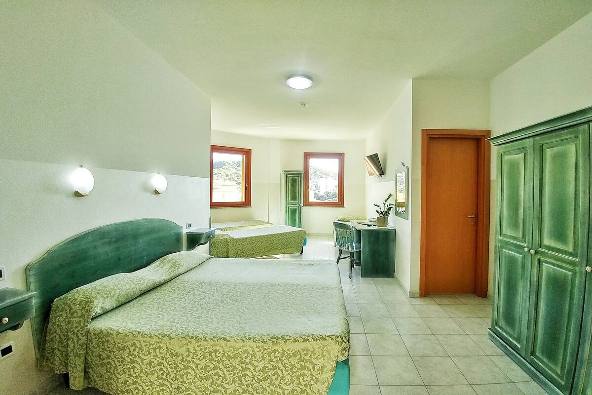 A hotel room with two beds, a desk, a wardrobe, and a view of the outside.