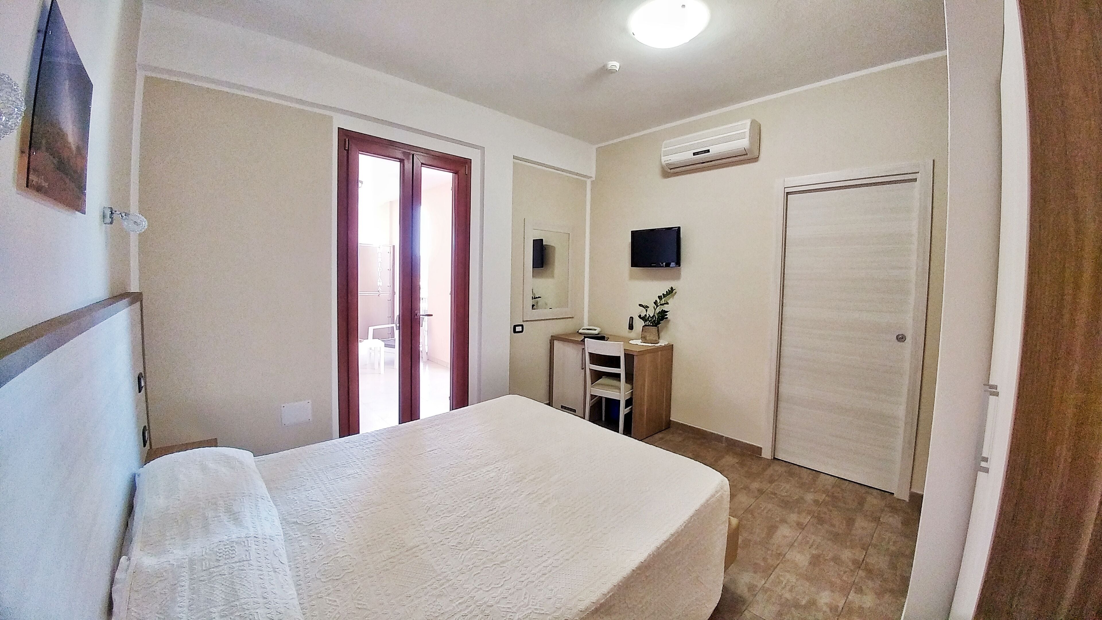 Ein Schlafzimmer mit Bett, Schreibtisch, Stuhl, Fernseher und Kleiderschrank.