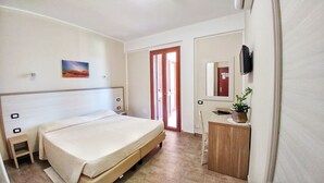 Habitación de hotel con cama, un pequeño escritorio con planta, espejo y un cuadro en la pared.