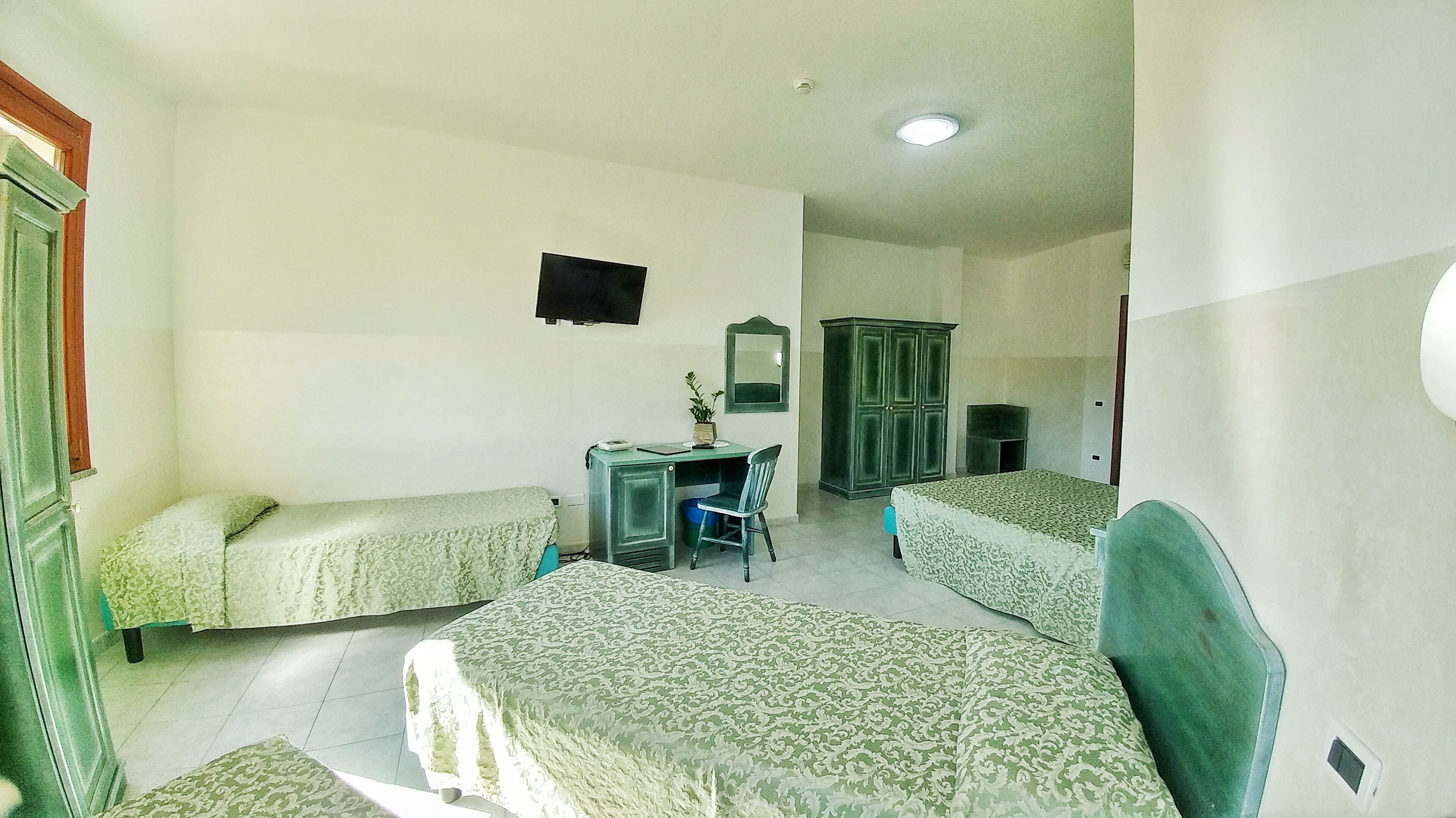 A room with two single beds, a desk with a chair, a television, and a wardrobe.