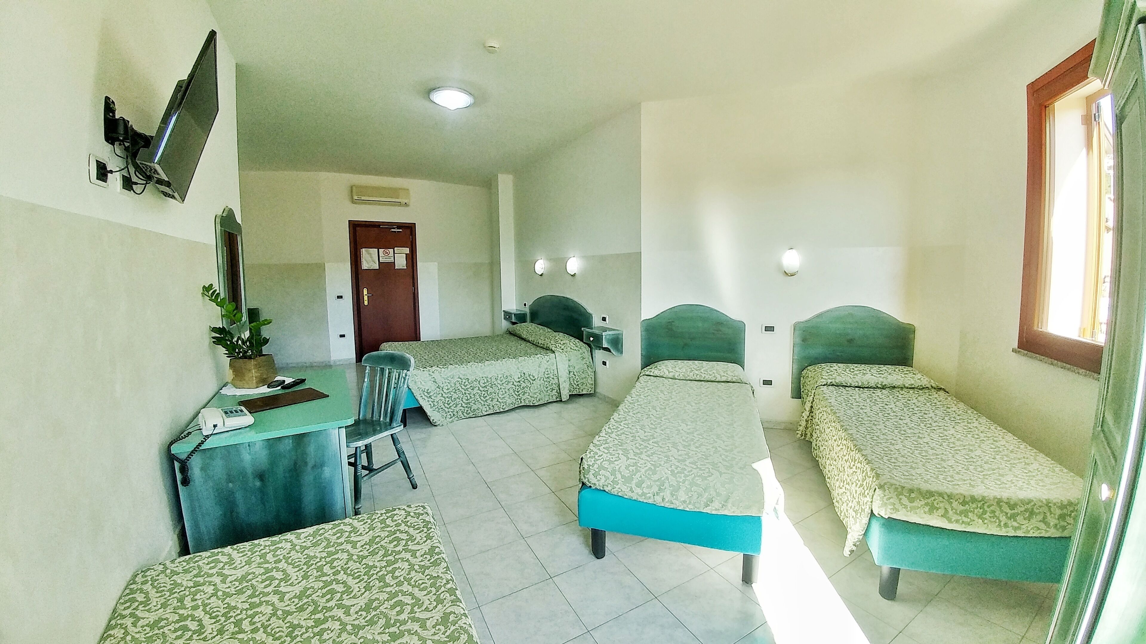 A room with two single beds, a desk with a chair, a TV, and a door.