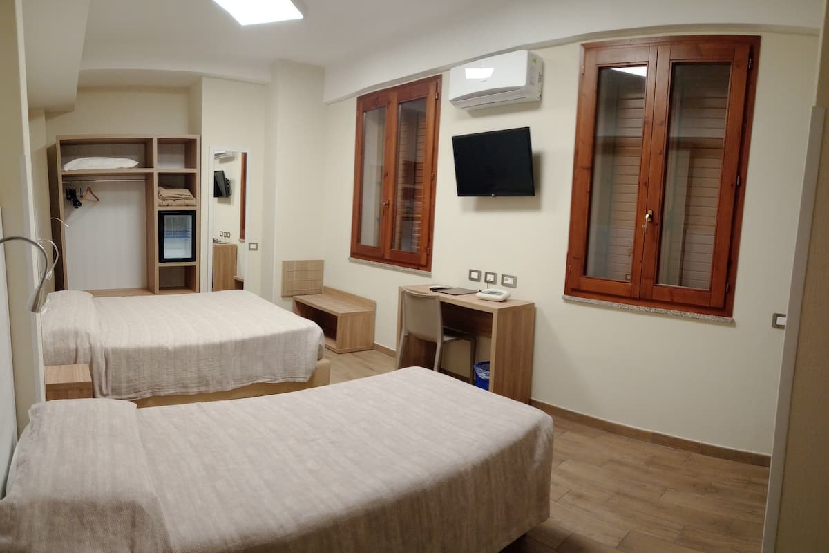 A hotel room with two beds, a desk, a chair, a TV, and a wardrobe.