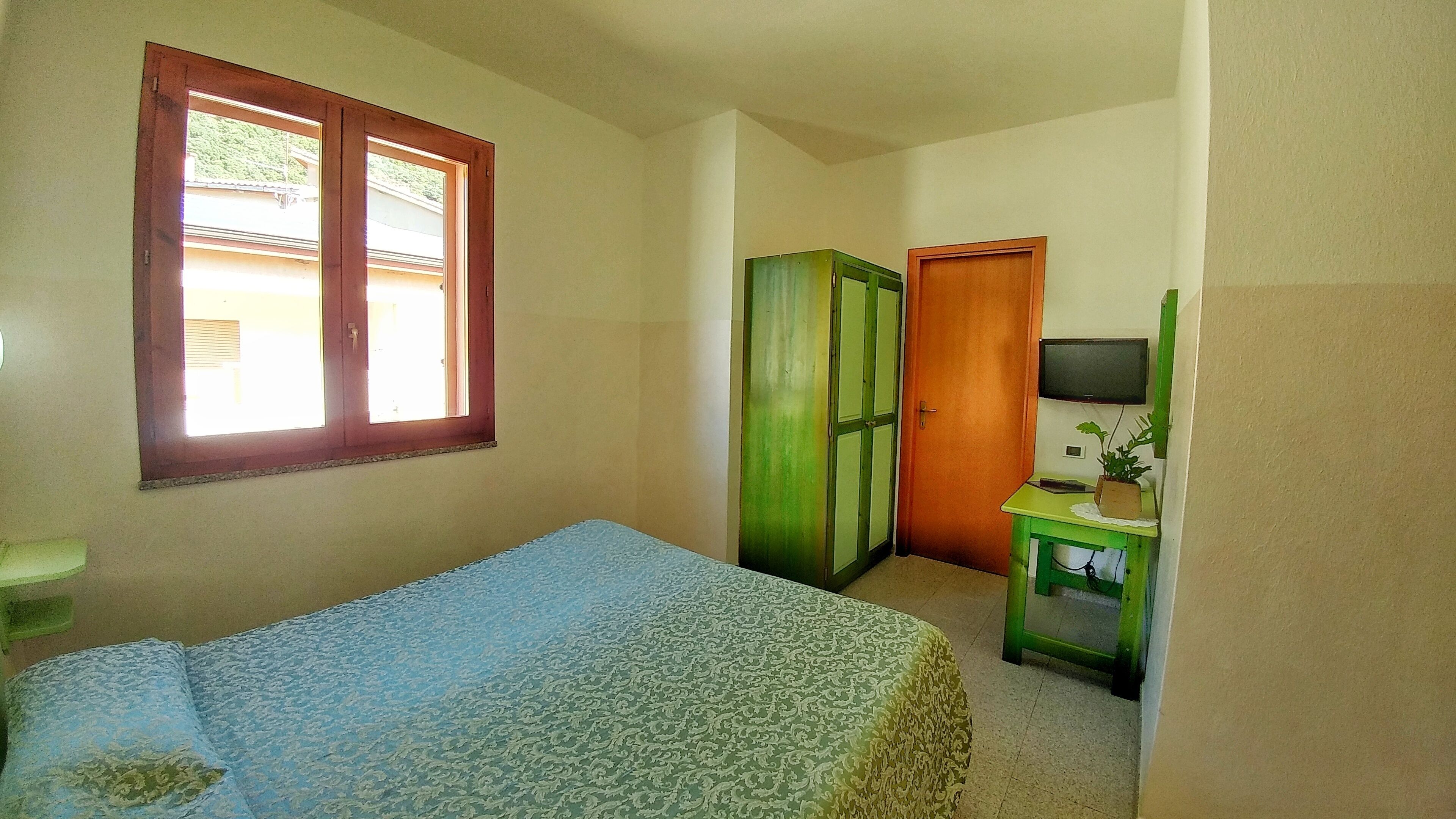 A bedroom with a bed, a wardrobe, a television on a stand, and a window.