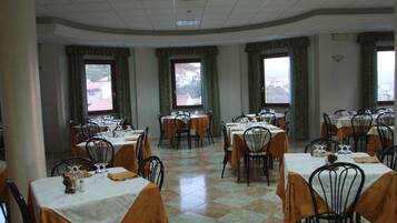 A dining area with tables set for service, large windows, and a tiled floor.