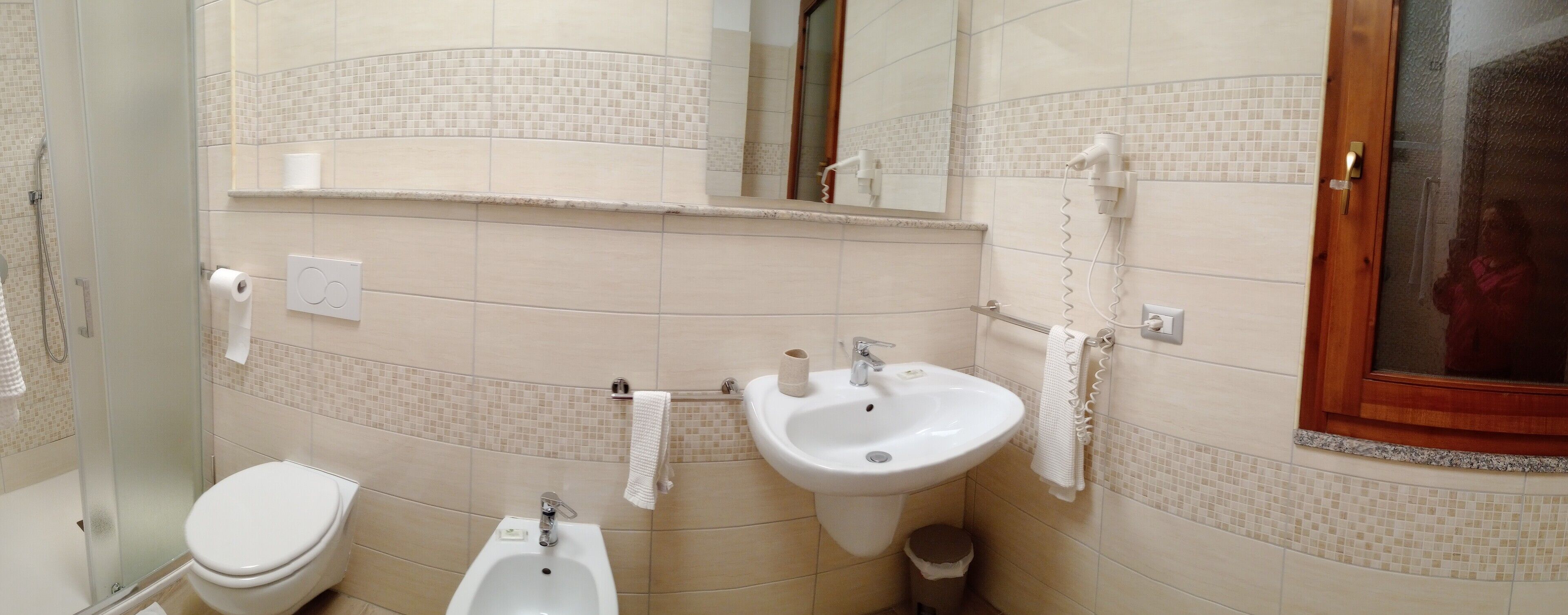 A bathroom with a toilet, bidet, and sink, tiled walls, and a mirror.