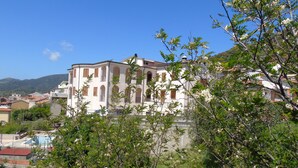 Un edificio grande con varios balcones y un patio central, rodeado de vegetación y otros edificios.