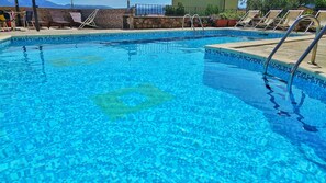A clear blue pool with tiled edges, lounge chairs, and a stone wall.