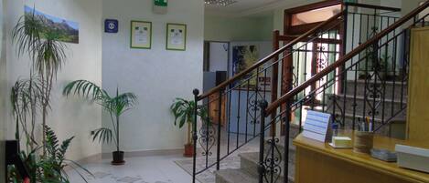 Un hall d’hôtel avec un escalier, des plantes en pot, des certificats encadrés accrochés au mur et un sol carrelé.