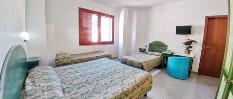 Una habitación con dos camas, un escritorio, un televisor y una ventana con contraventanas rojas.