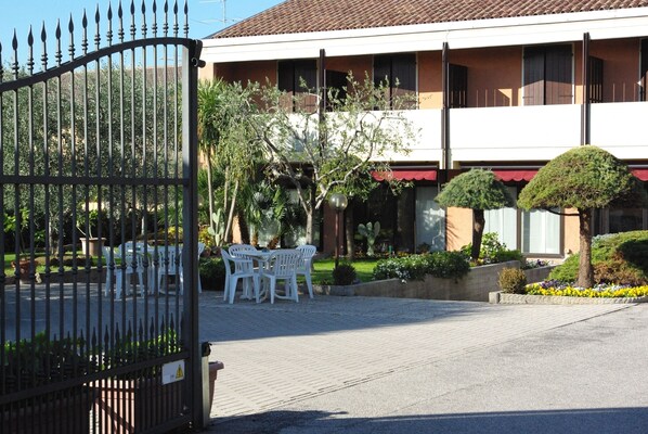 A gated entrance with a paved area, a building with a tiled roof, and a small garden with chairs and plants. - Hotel Andreis (Cavaion Veronese)