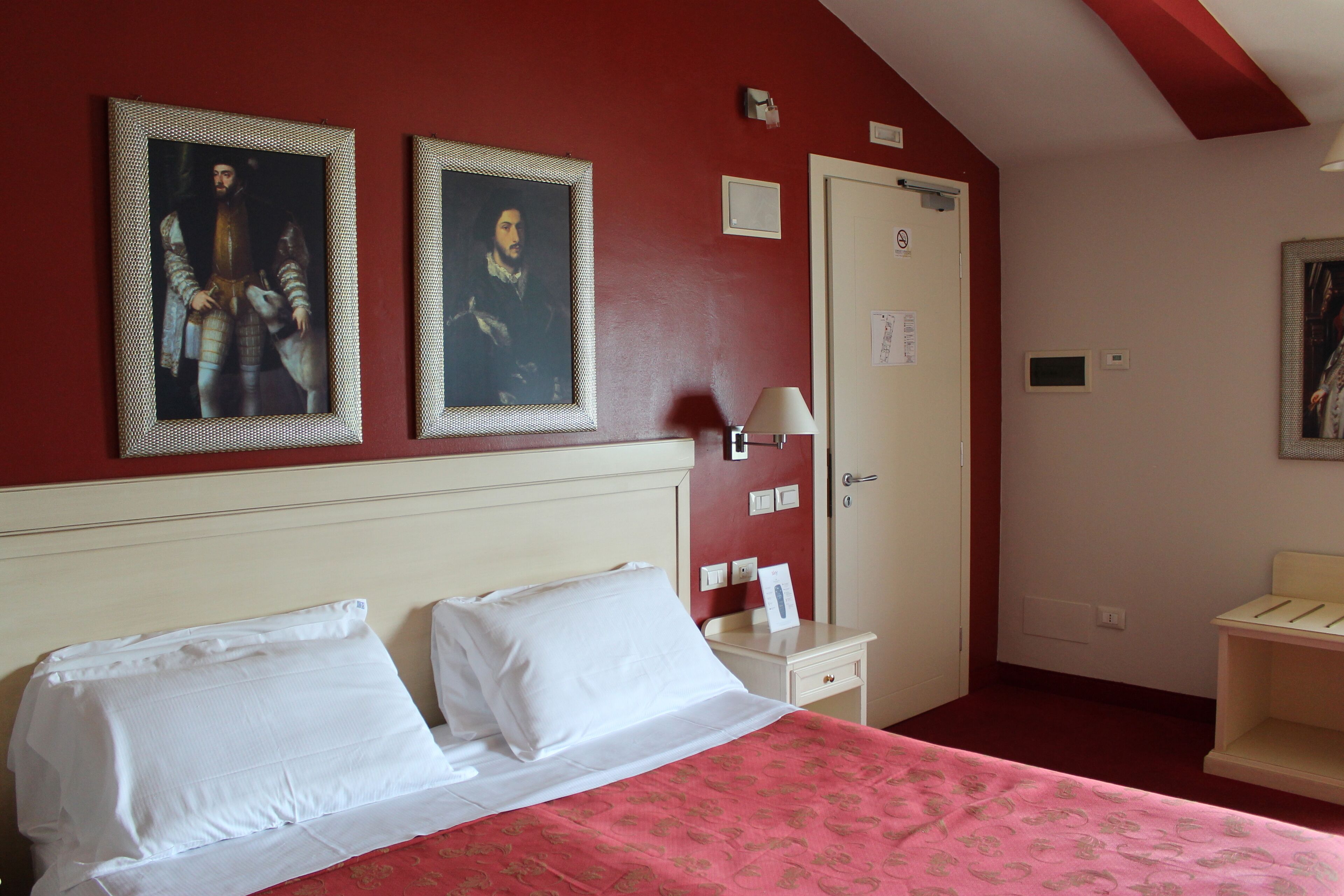 A hotel room with a bed, a nightstand, a lamp, and two framed pictures on the wall.