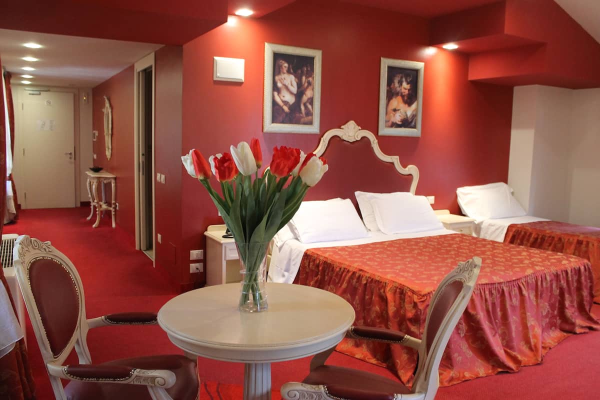 A hotel room with two beds, a dining table with chairs, and a vase of red and white tulips.