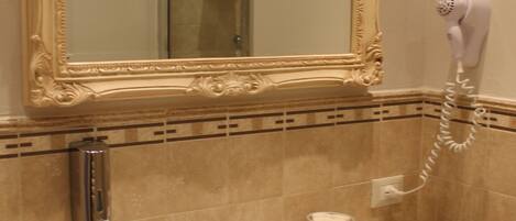 Un baño con un espejo grande y decorativo, un lavabo blanco, un secador de pelo de mano y una toalla colgada en un perchero.