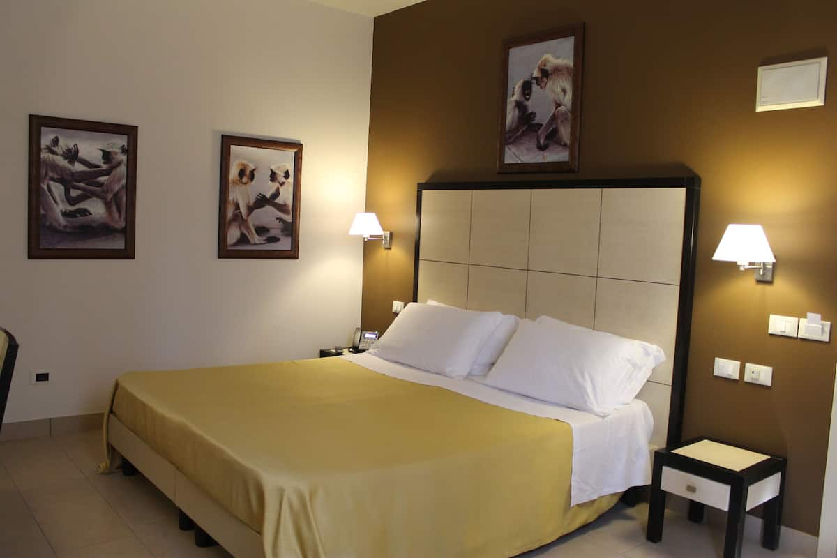 A hotel room with a large bed, two bedside lamps, a nightstand, and two framed pictures on the wall.