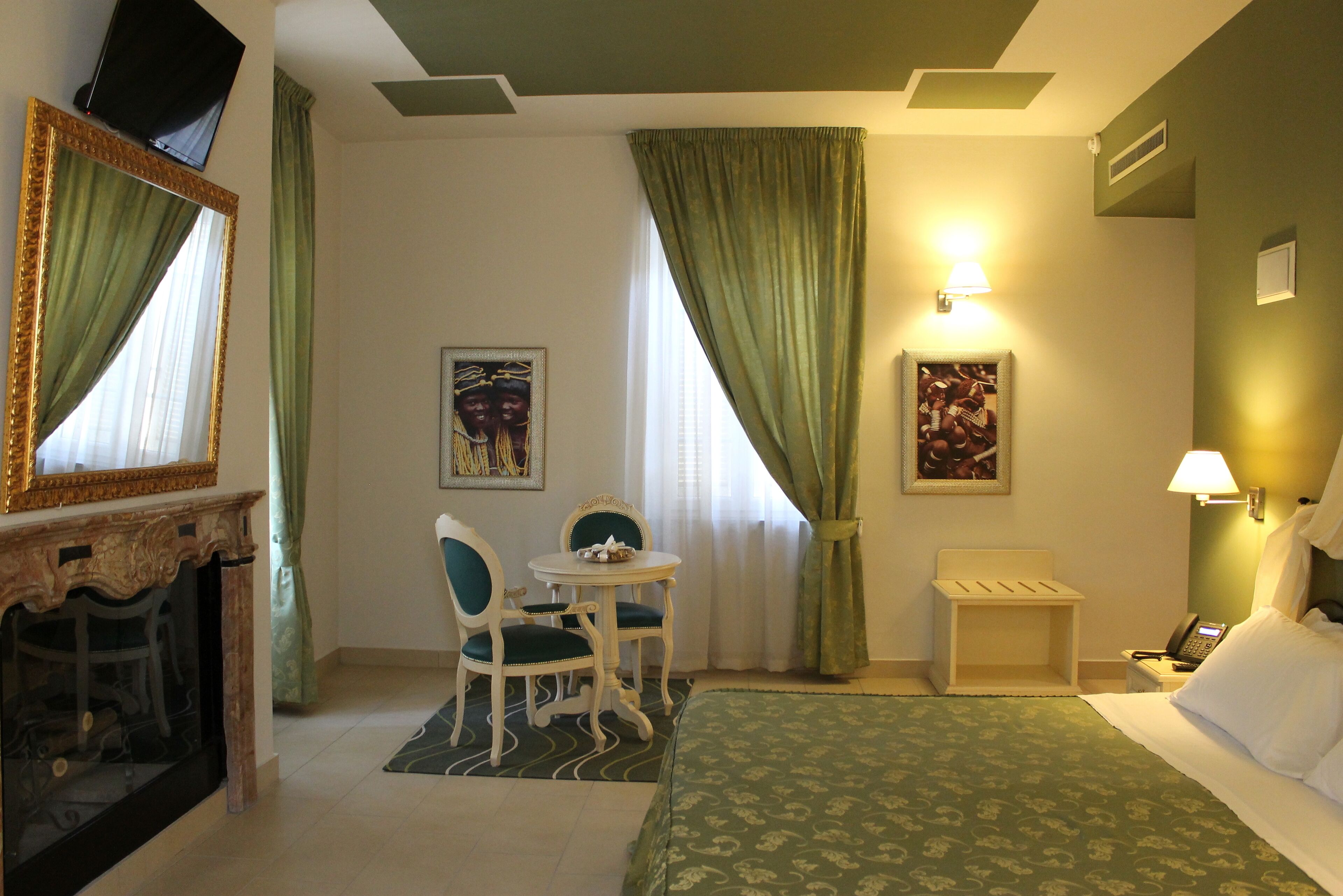 Habitación de hotel con cama, escritorio con dos sillas, una mesita, chimenea y dos lámparas de pared.