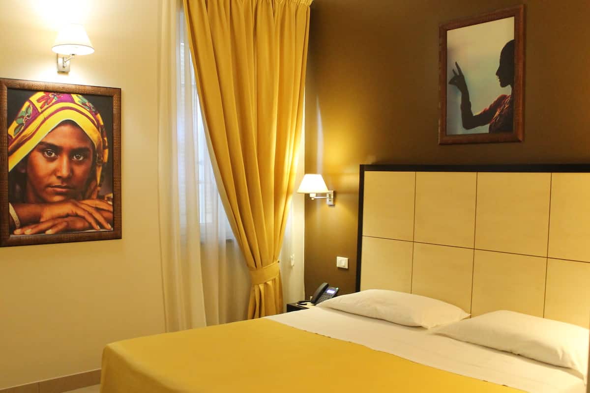 A hotel room with a bed, a nightstand, a lamp, a painting, and a curtain.