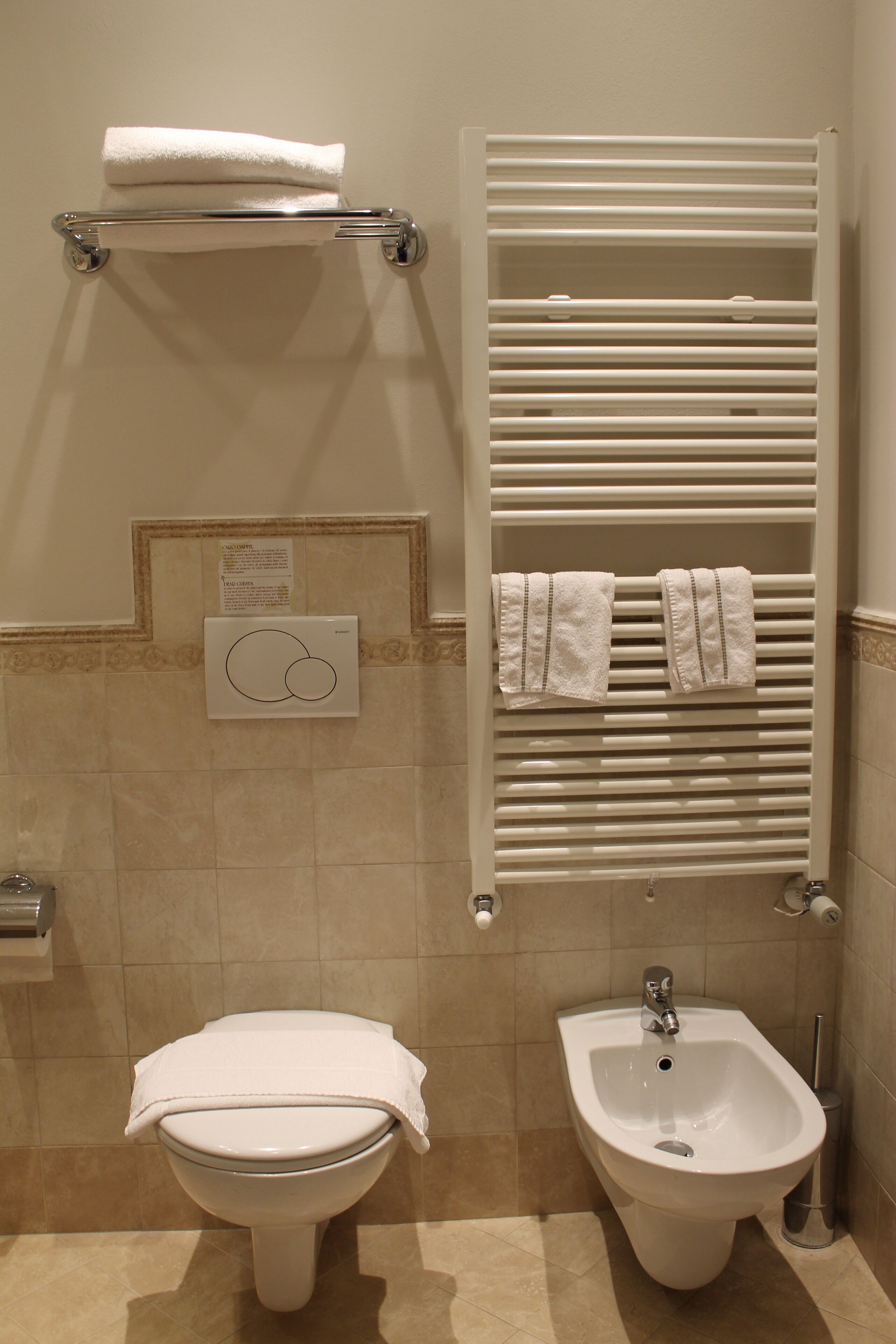 A bathroom with a toilet, bidet, towel rack, and a wall-mounted towel warmer.