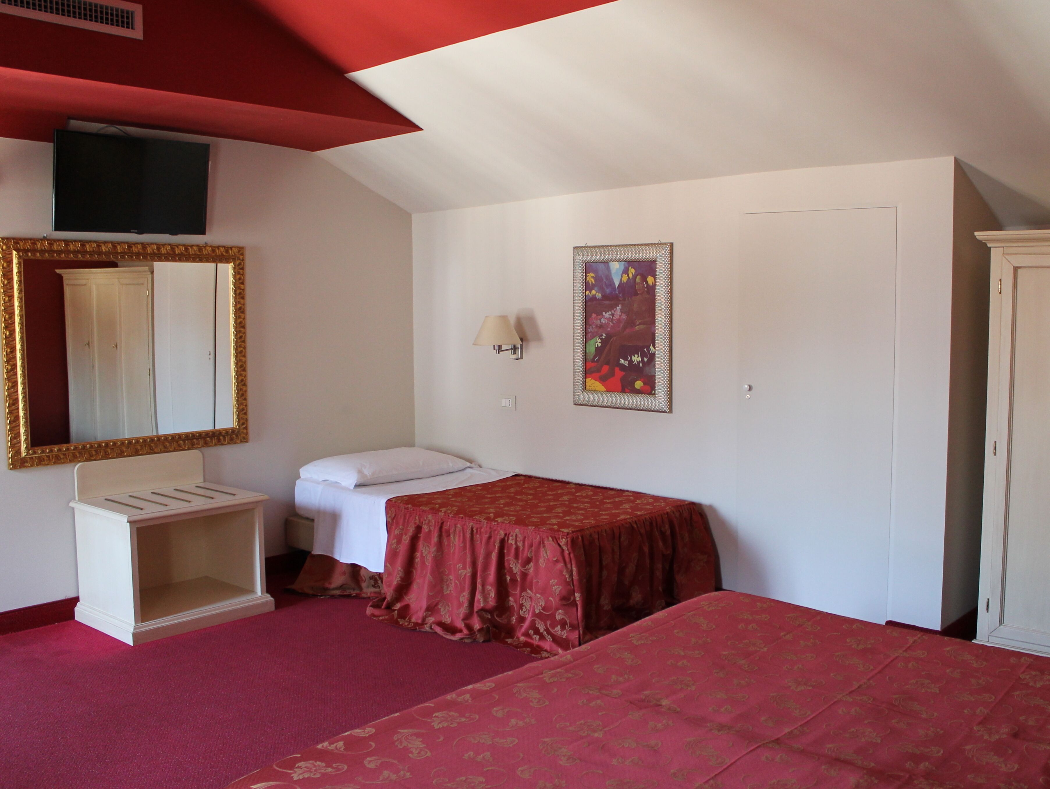 A bedroom with a bed, a wardrobe, a mirror, a toilet, and a wall-mounted TV.
