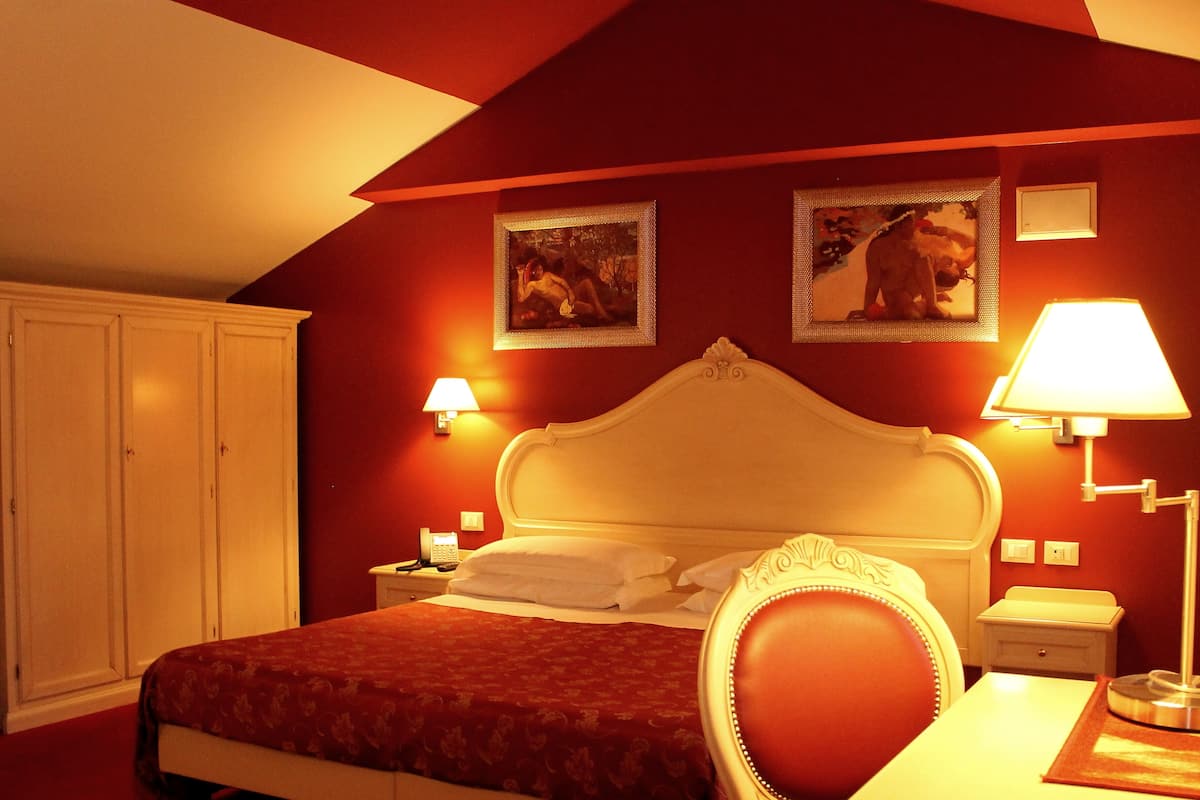 A hotel room with a large bed, a nightstand, a desk, and two wall-mounted lamps.