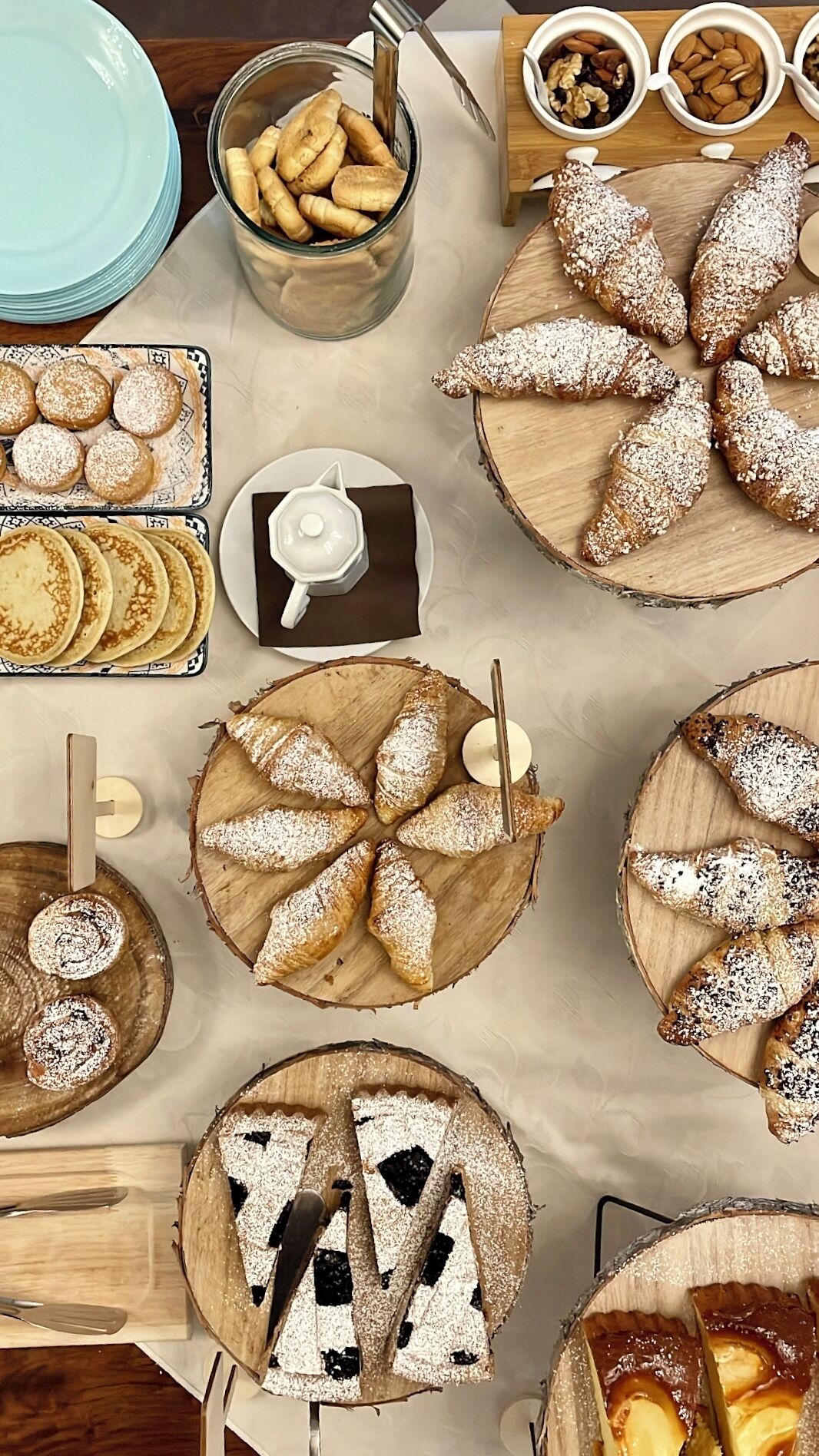 Variedad de pasteles y postres sobre tablas de madera, junto con una tetera blanca pequeña y un plato de galletas.