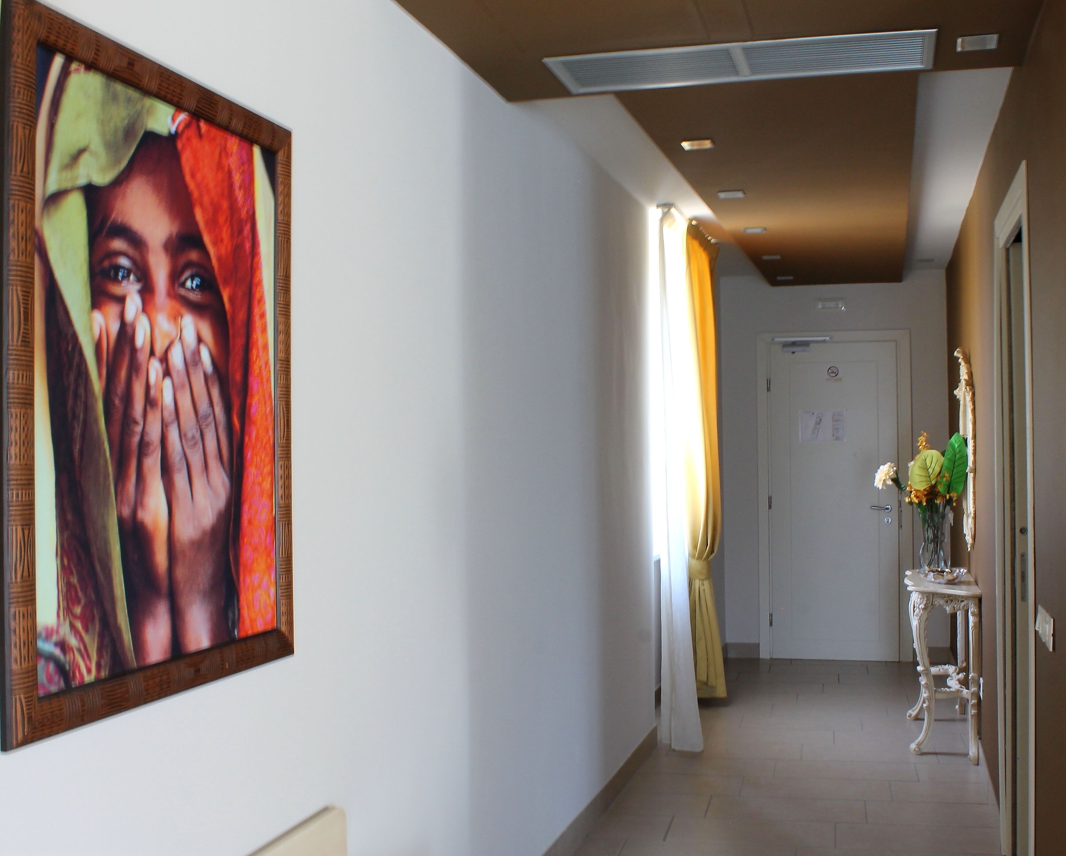 A hallway with a framed artwork on the wall, a door with a sign, and a table with a vase of flowers.