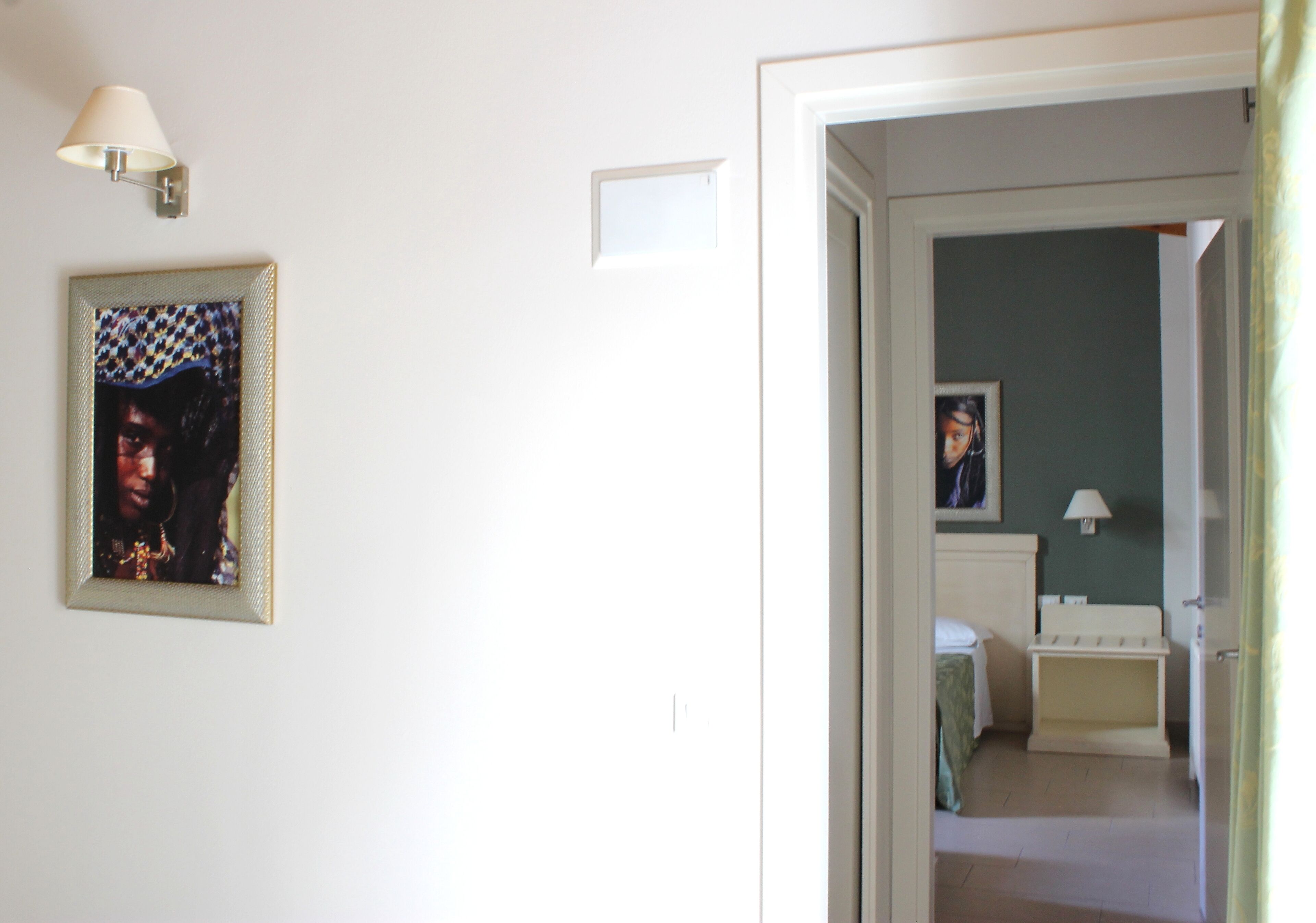Um corredor com um quadro na parede, uma mesa de cabeceira e uma cama no quarto vizinho.