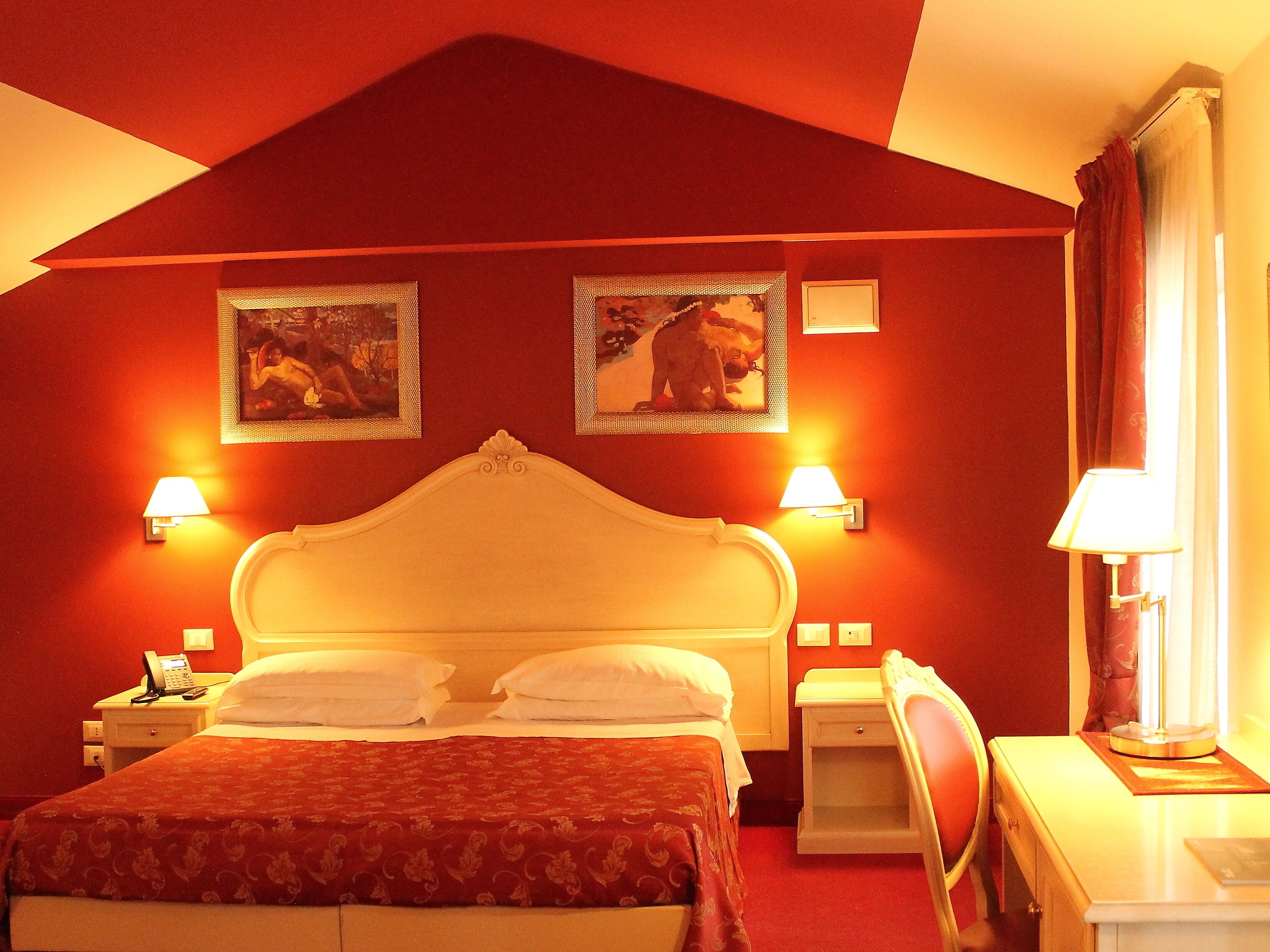 Ein Hotelzimmer mit einem großen Bett, zwei Wandlampen, einem Telefon und einem Schreibtisch mit Lampe.