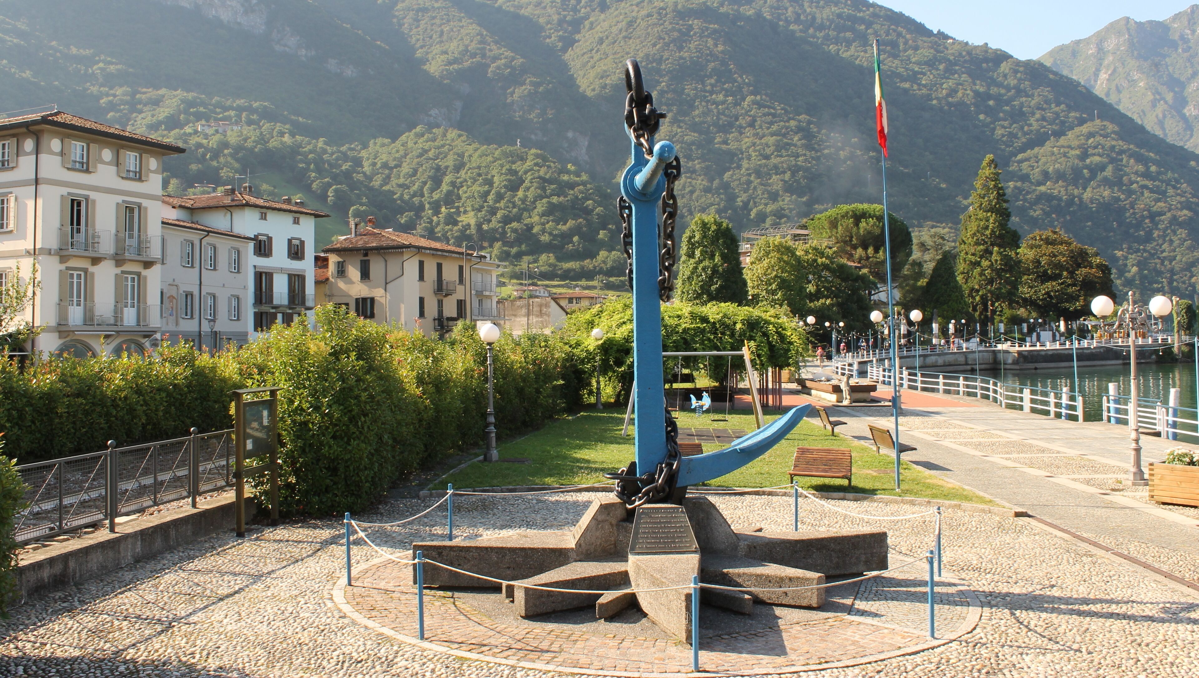 Un parco con una scultura blu, panchine in pietra e vista su un lago.