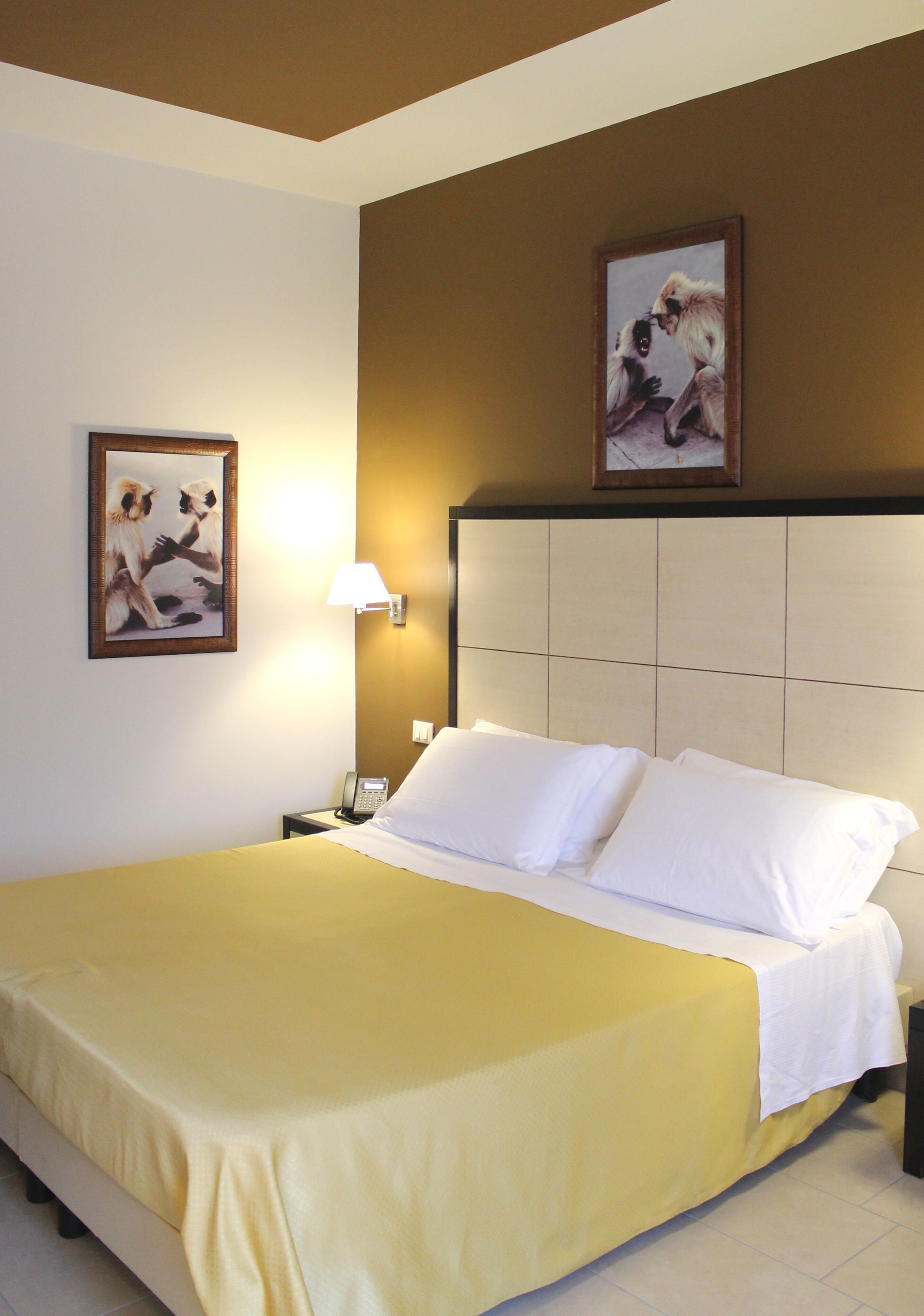 A hotel room with a large bed, a nightstand with a lamp, and two framed pictures on the wall.