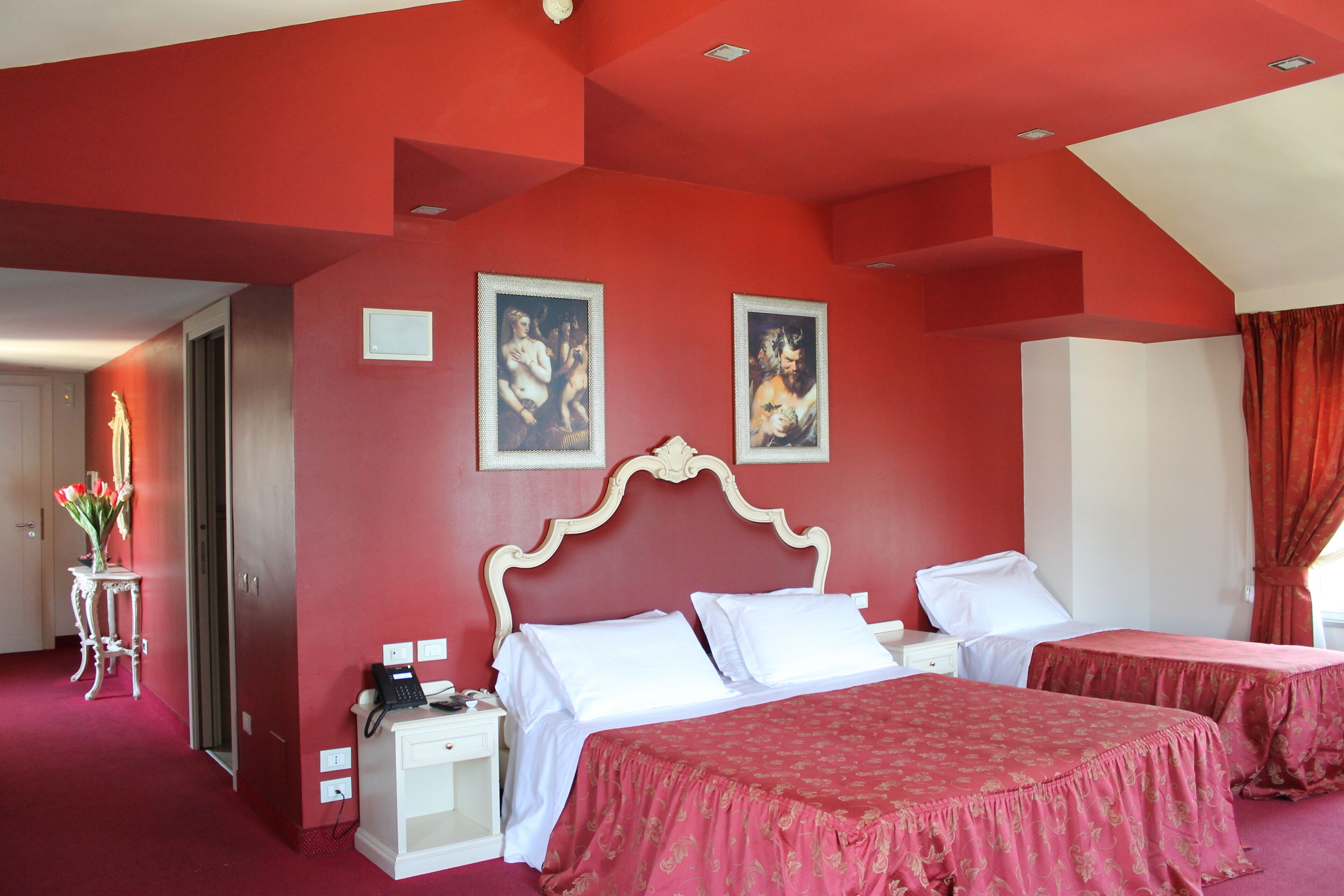 Une chambre d’hôtel avec deux lits, un mur d’accent rouge et des œuvres d’art au-dessus des lits.