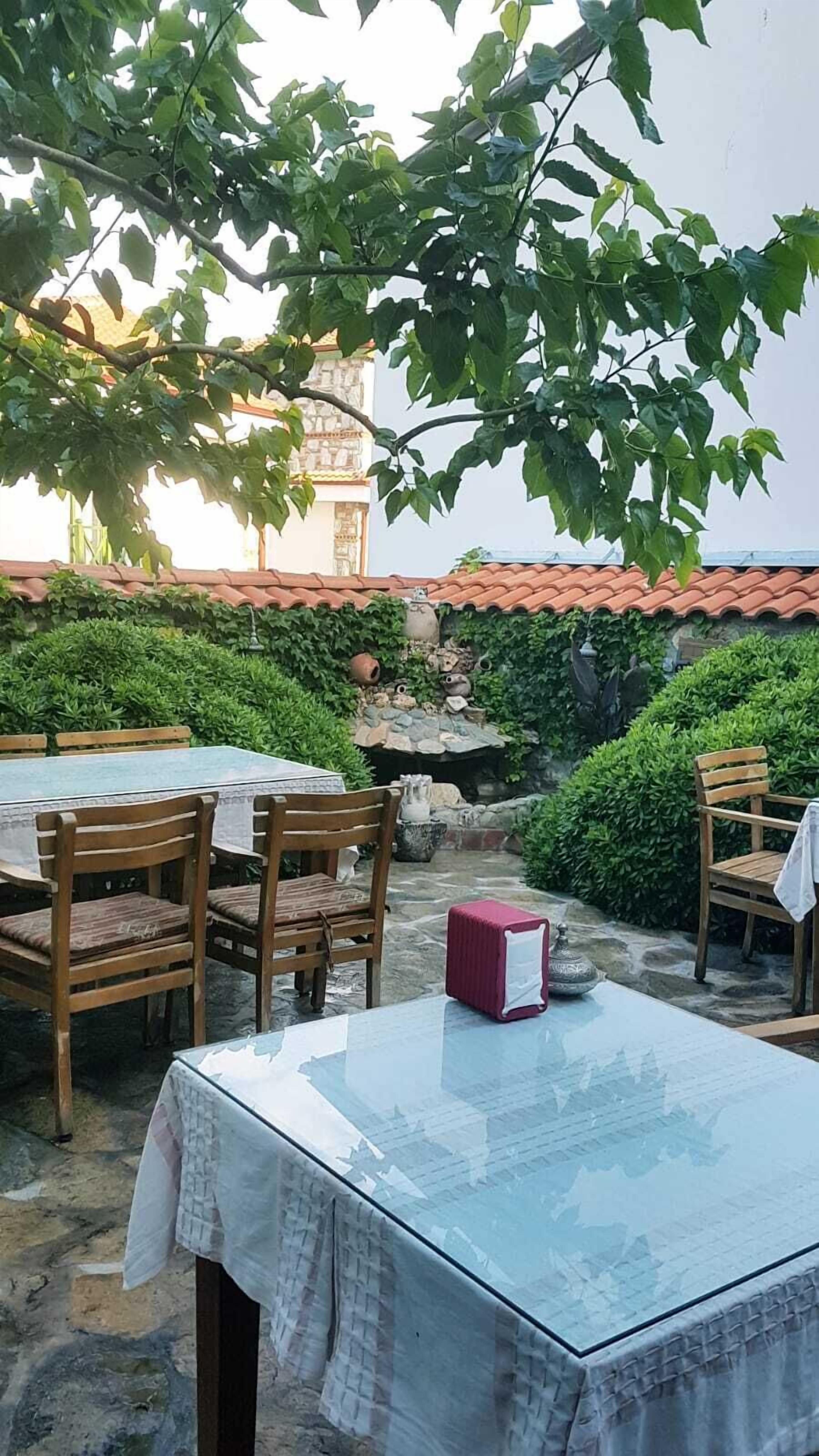 Un espace de restauration en plein air doté d’un sol en pierre, de tables et de chaises en bois, et offrant une vue sur un bâtiment dont le toit est recouvert de tuiles.