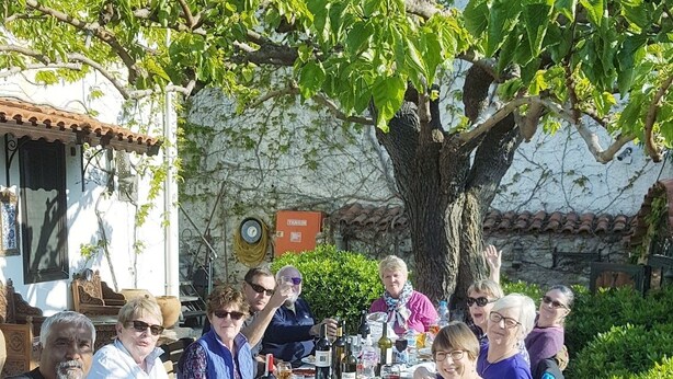 A group of people seated around a table outdoors, with a tree and a building in the background. - Hotel Nilya - Special Class (Selçuk)