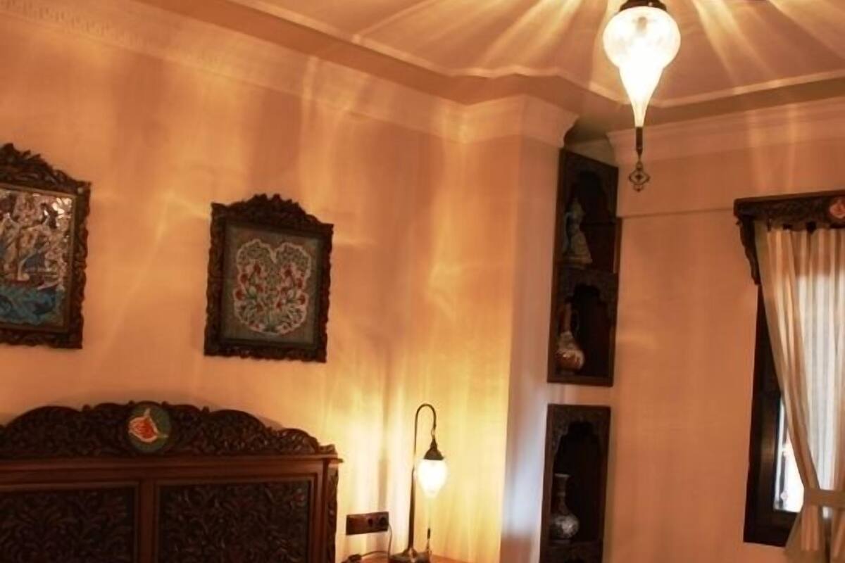 Un dormitorio con una cama grande, un cabecero de madera, una mesita de noche con una lámpara y una lámpara de techo.