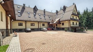 En bygning med tegltag, flere vinduer og en belagt gårdsplads med parkerede biler.