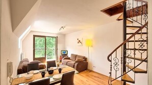 En hyggelig stue med spisebord, stole, sofa, fjernsyn og trappe.