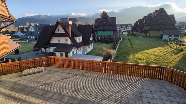 A residential area with traditional houses, a wooden fence, and a mountainous backdrop. - VISITzakopane Rainbow Apartments (Zakopane)