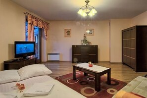 A hotel room with a bed, a TV, a small table, a wardrobe, and a chandelier.