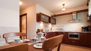 A kitchen with wooden cabinets, a stove, and a dining table set with tea cups and plates. - VISITzakopane Rainbow Apartments (Zakopane)
