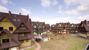 A row of traditional chalet-style buildings with pitched roofs and dormer windows, arranged in a linear fashion with a grassy courtyard in the center. - VISITzakopane Rainbow Apartments (Zakopane)