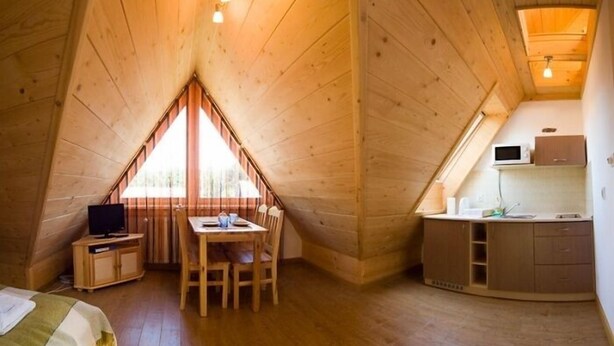 A cozy, wooden-paneled room with a dining table, chairs, a TV, and a kitchenette. - VISITzakopane City Apartments (Zakopane)