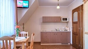 A compact kitchen with wooden cabinets, a microwave, and a dining area with a table and chairs. - VISITzakopane City Apartments (Zakopane)